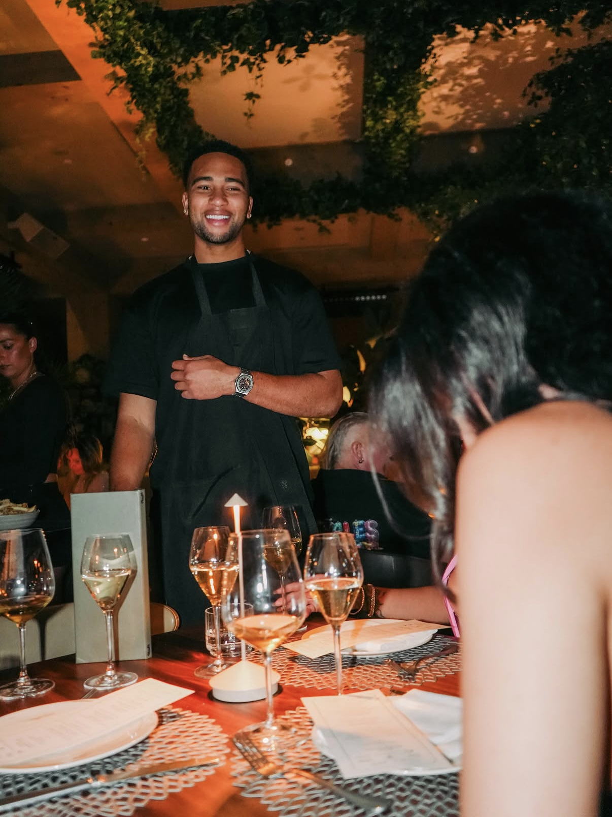 An NFL player in a Celebrity Waiter Night apron greeting guests at the table.